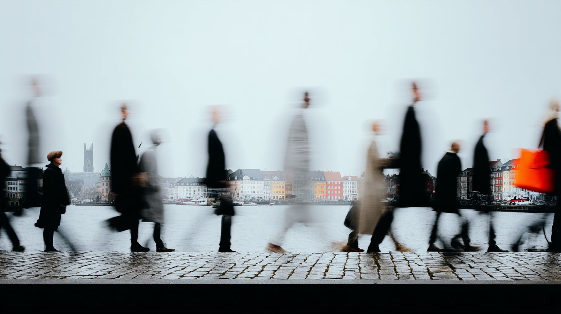 Mennesker i bevægelse langs en havnefront i nordisk dagslys